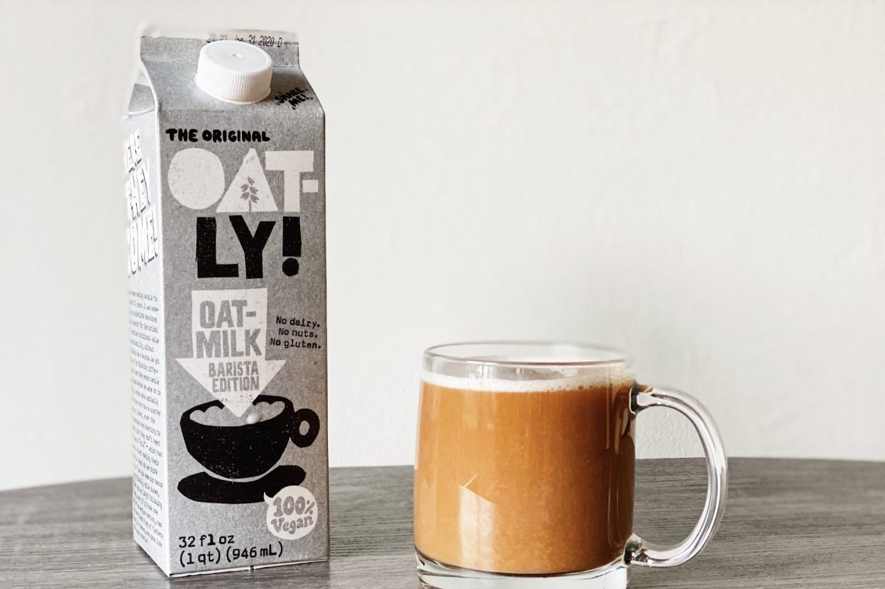 An Oatly milk carton next to a cup of coffee.